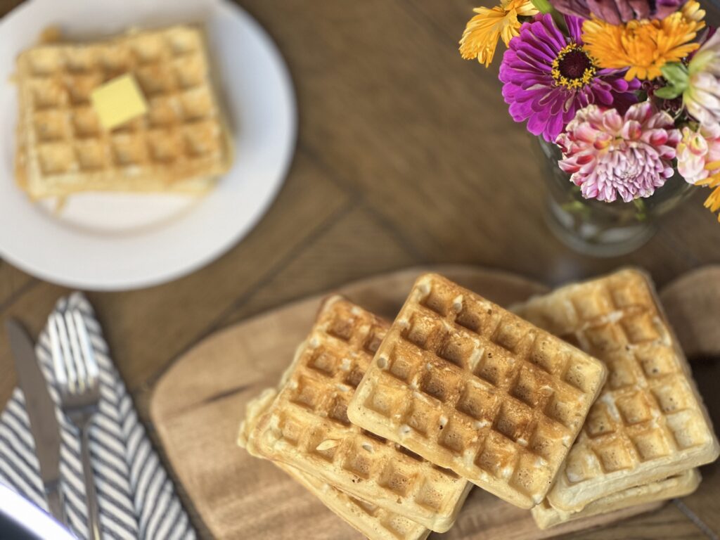 Best Sourdough Discard Waffles [Egg Free, Dairy Free, Vegan]. Stacks of delicious waffles, and a pretty vase of flowers.